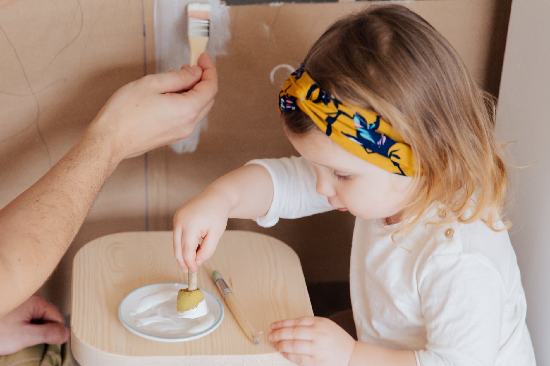 girl in white long sleeve shirt holding sponge with paint