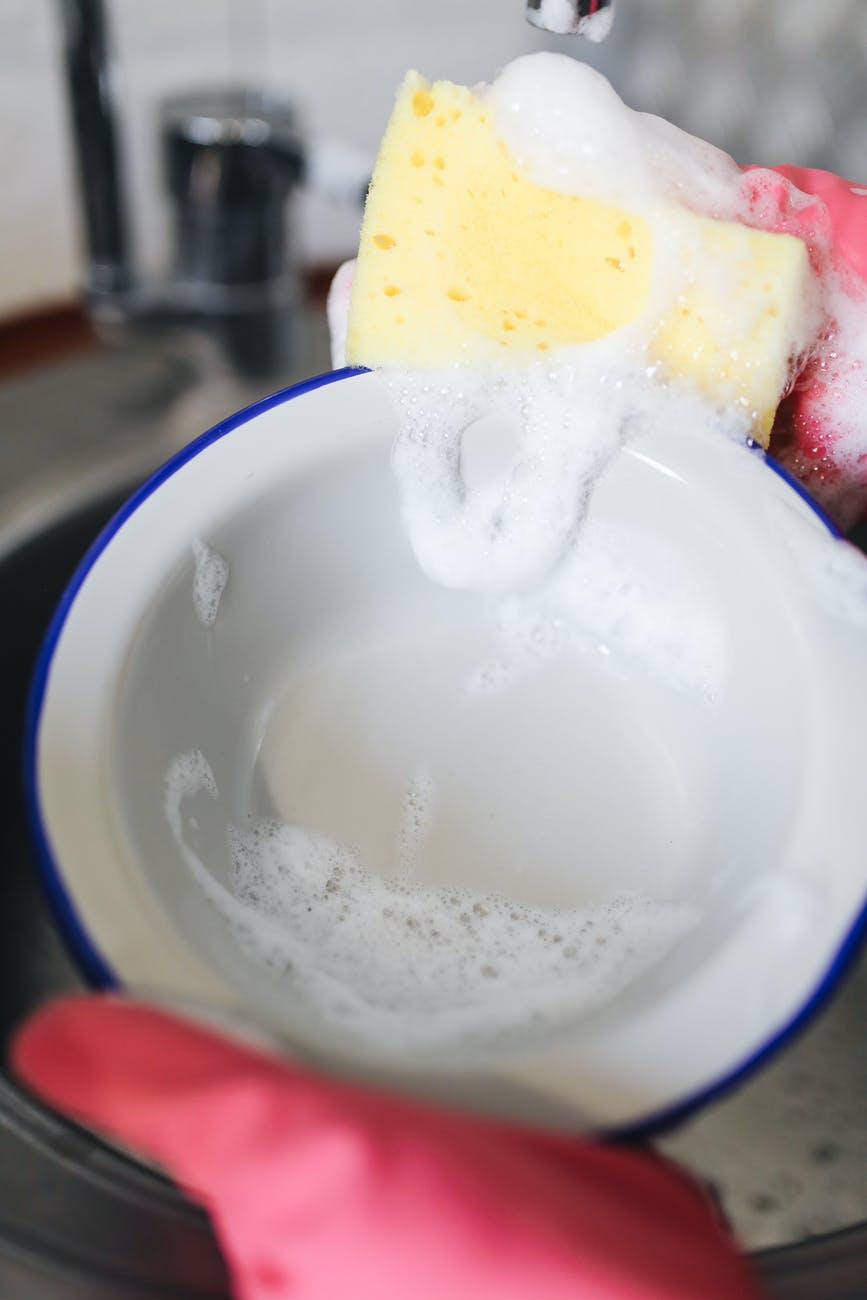 a person wearing rubber gloves washing a white bowl