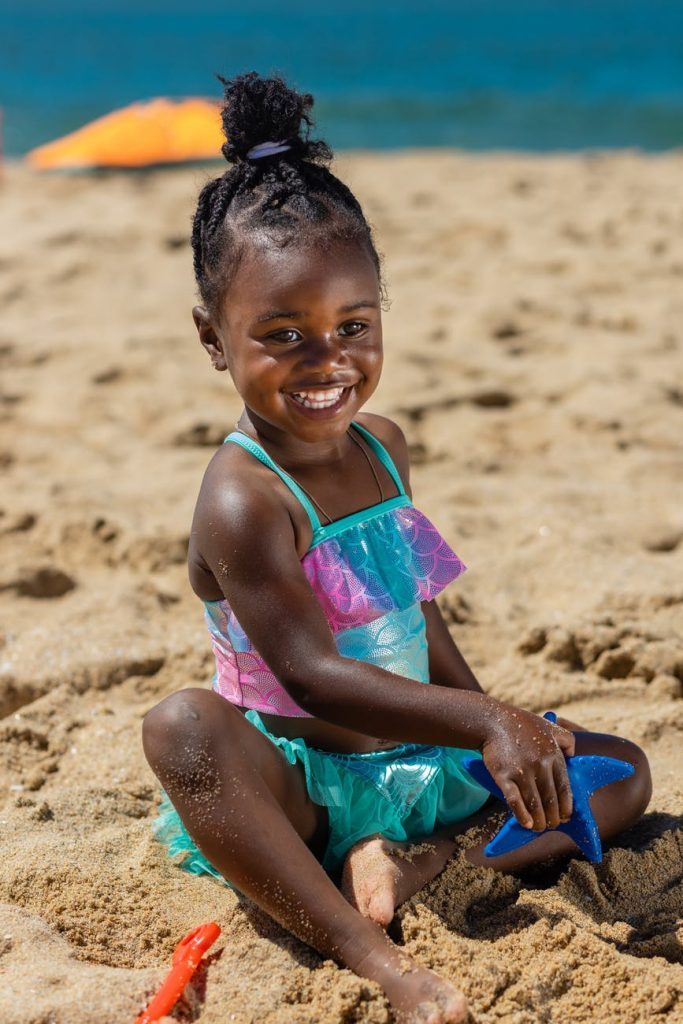 a young girl sitting on the sand while holding her toy